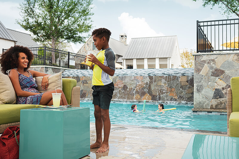 Family relaxing near swimming pool at amenity center in The Grove Frisco